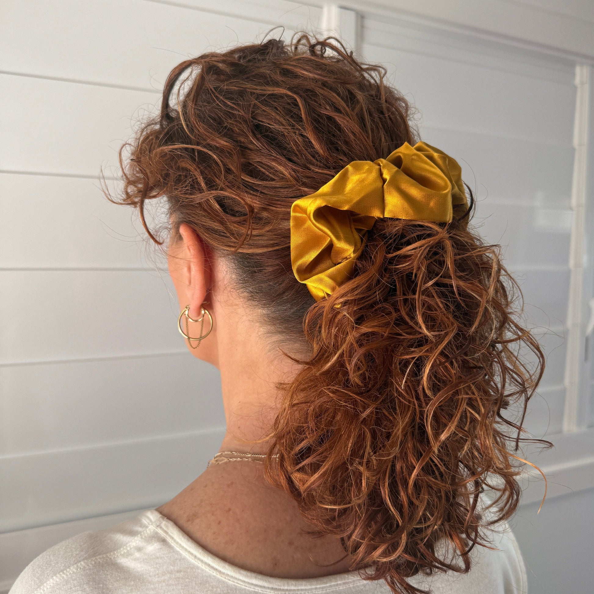 Person with curly hair wearing a gold scrunchie, standing against a white background